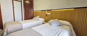 Habitación de hotel con dos camas individuales, un panel de pared de madera, una mesita de noche con lámpara y un teléfono.