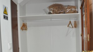 Un armario espacioso con puerta de madera, un estante blanco y un pequeño cajonero blanco.