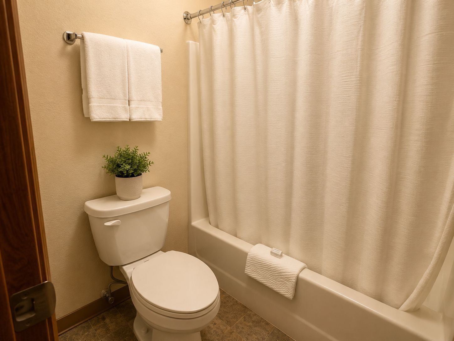 Une salle de bain avec des toilettes, une plante en pot, une baignoire et un rideau de douche.