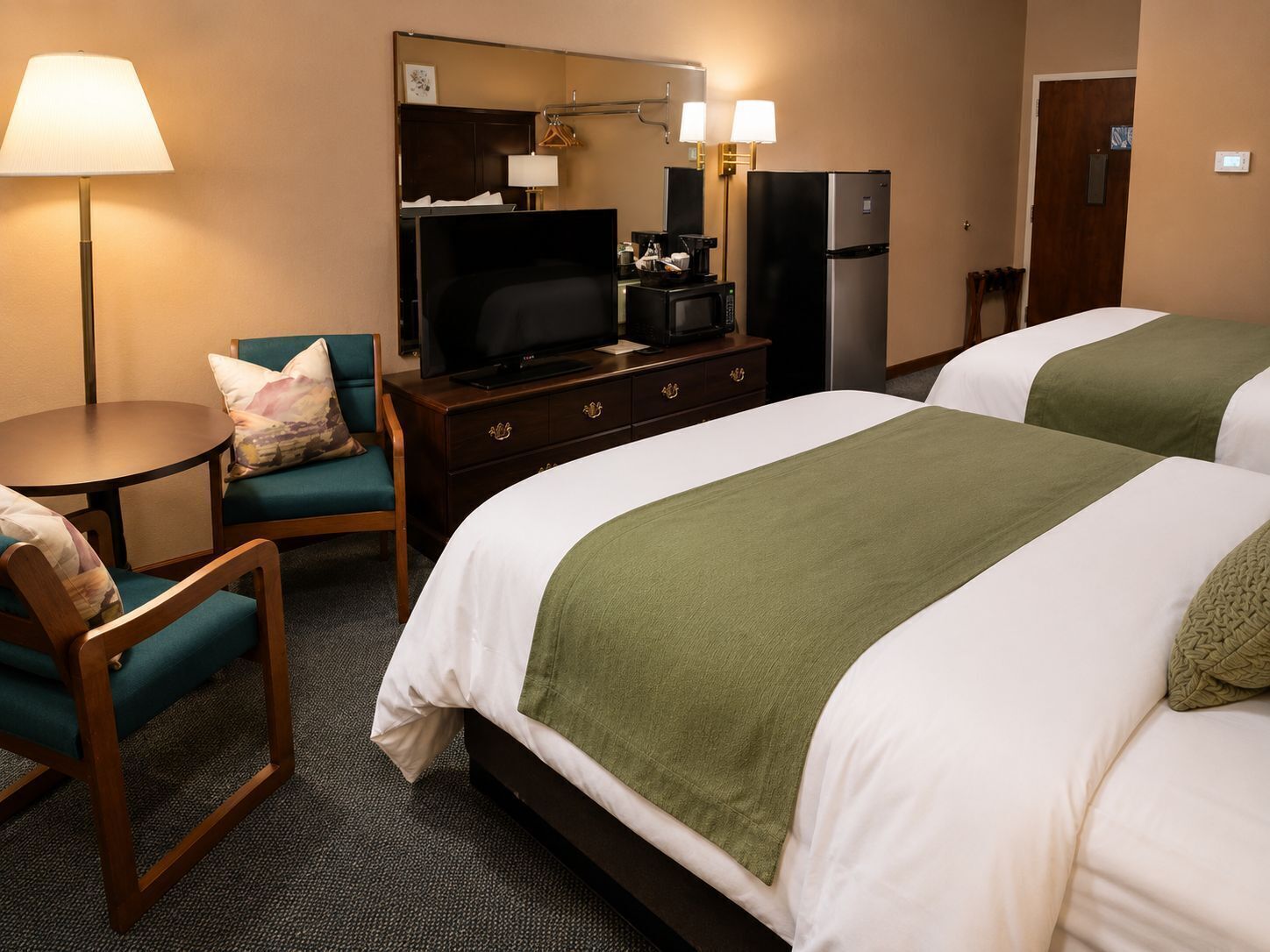 Une chambre d’hôtel avec deux lits, un bureau avec une télévision, un réfrigérateur et une lampe.