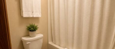 A bathroom with a toilet, a potted plant, a towel hanging on a rack, and a shower curtain.