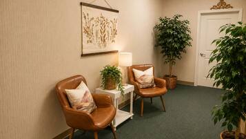 A room with two leather chairs, a small table with a lamp, a wall-mounted artwork, and two potted plants.