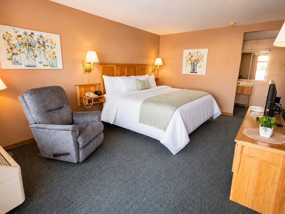 Een hotelkamer met een bed, een stoel, een bureau en twee wandlampen.