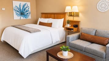 A hotel room with a bed, a sofa, a nightstand with lamps, a wall clock, and a painting.