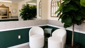 A bathroom with two white chairs, a potted plant, and a mirror reflecting the room.