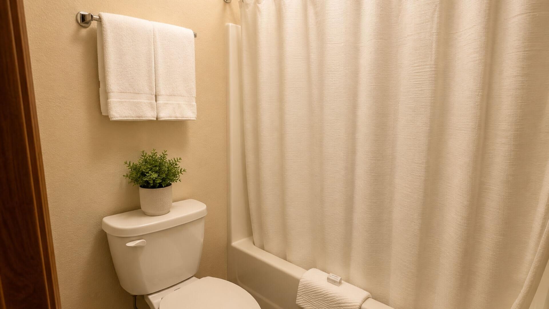 A bathroom with a toilet, a potted plant, a towel, and a shower curtain.