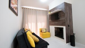 Una sala de estar con un sofá negro, cojines amarillos, un reposapiés amarillo, una chimenea y un cuadro enmarcado en la pared.