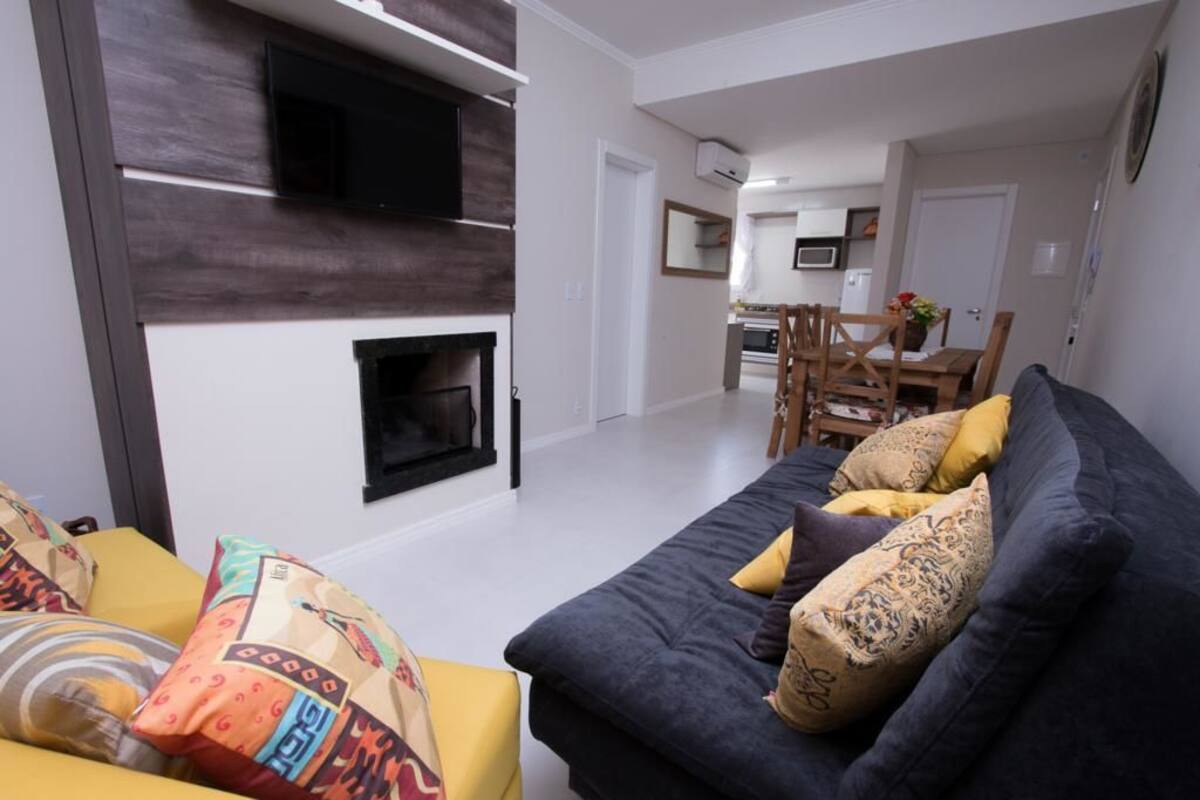 A living room with a dark sofa, yellow armchair, and colorful cushions. A fireplace is visible in the background.