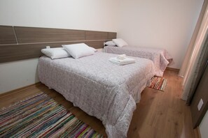 A hotel room with two beds, a wooden headboard, and a colorful striped rug. - Residencial Onze-1 (Gramado)