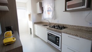 Una cocina moderna con armarios blancos, estufa a gas, horno, microondas y una ventana con cortina blanca.