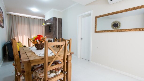 Un comedor con una mesa y sillas de madera, un jarrón de flores y una cocina al fondo.