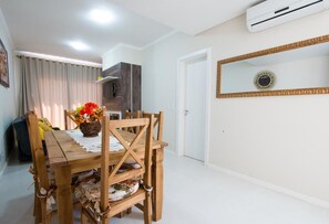 A dining area with a wooden table and chairs, a vase of flowers, and a kitchen in the background. - Residencial Onze-1 (Gramado)