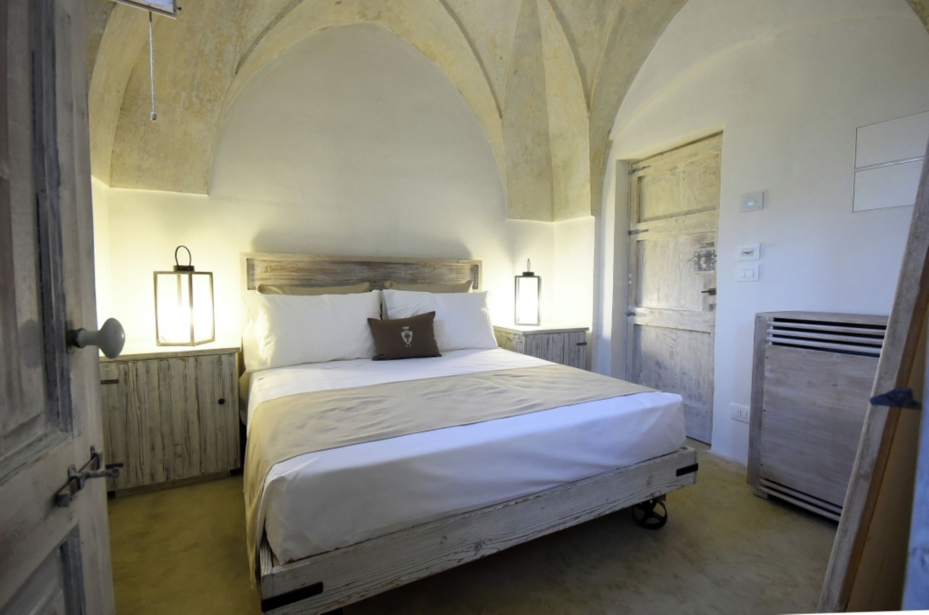 Una camera da letto con un letto in legno, lenzuola bianche e due lampade a parete.