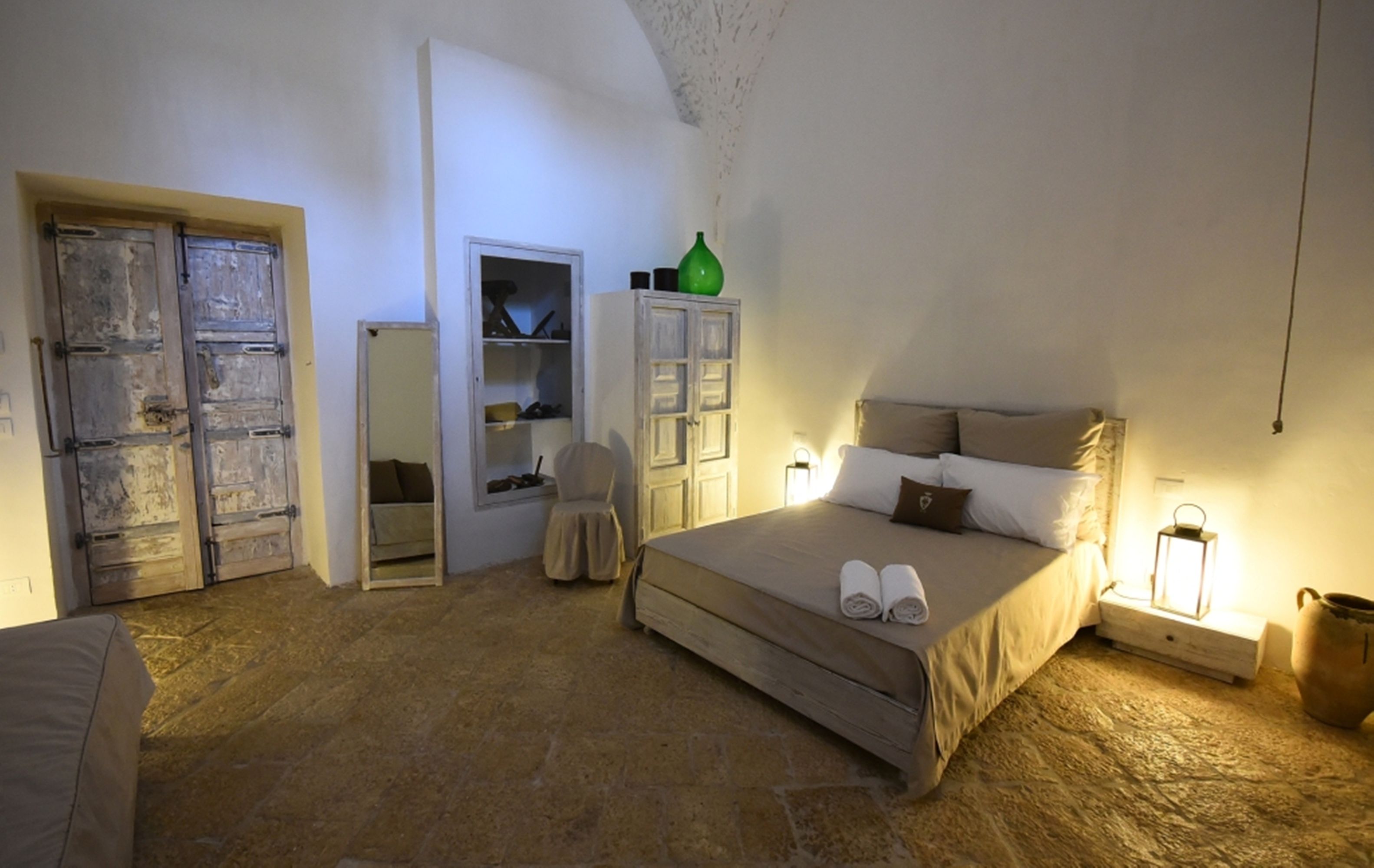 Un dormitorio con cama, armario, silla y mesita de noche con una lámpara.