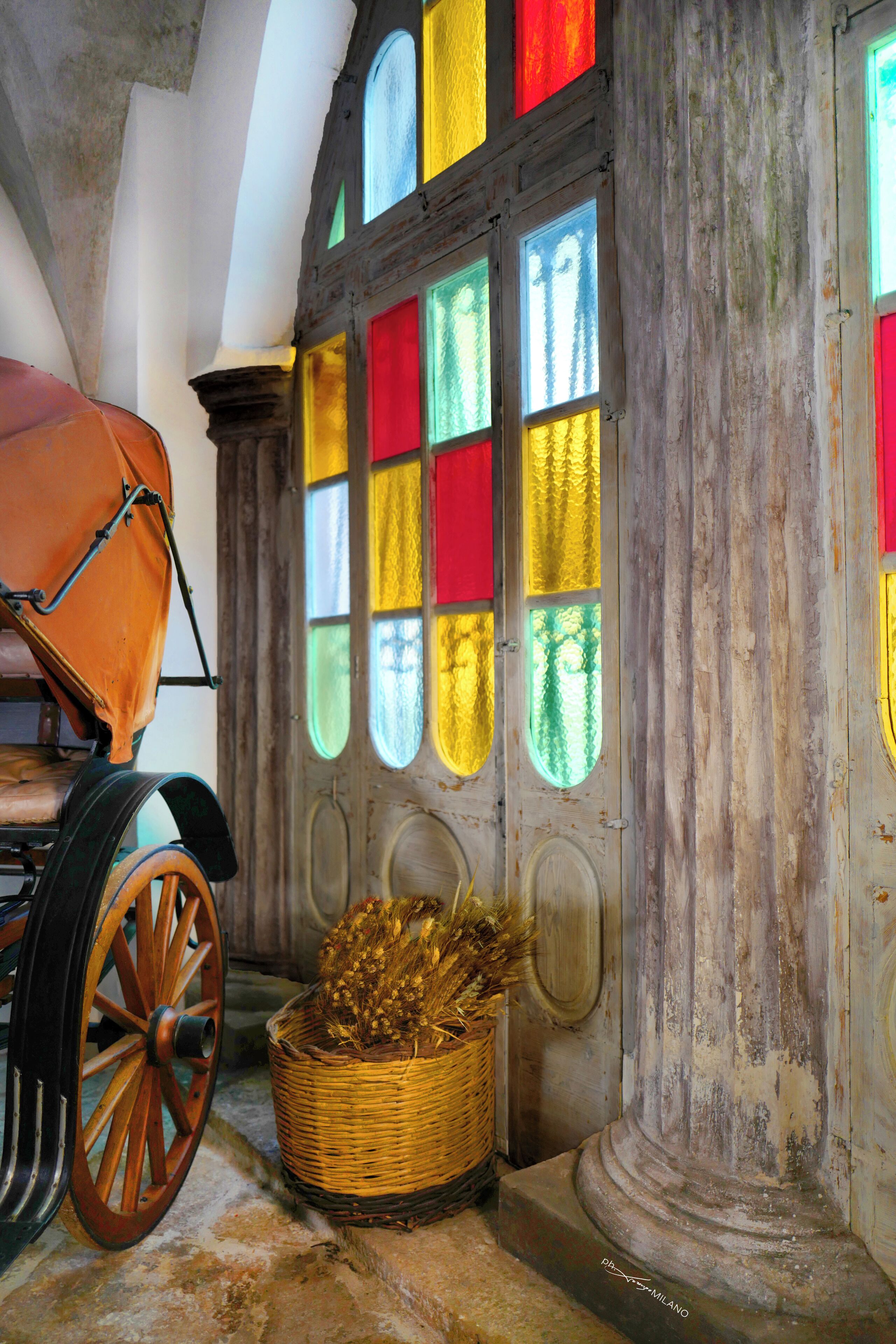 Un interior rústico con una puerta de madera, una cesta de mimbre y un carruaje antiguo.