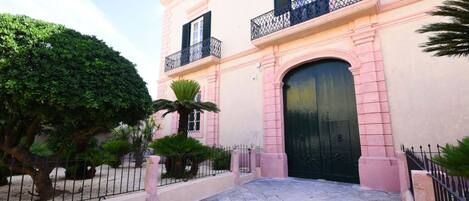 Un edificio con facciata rosa, cancello nero e ingresso lastricato.