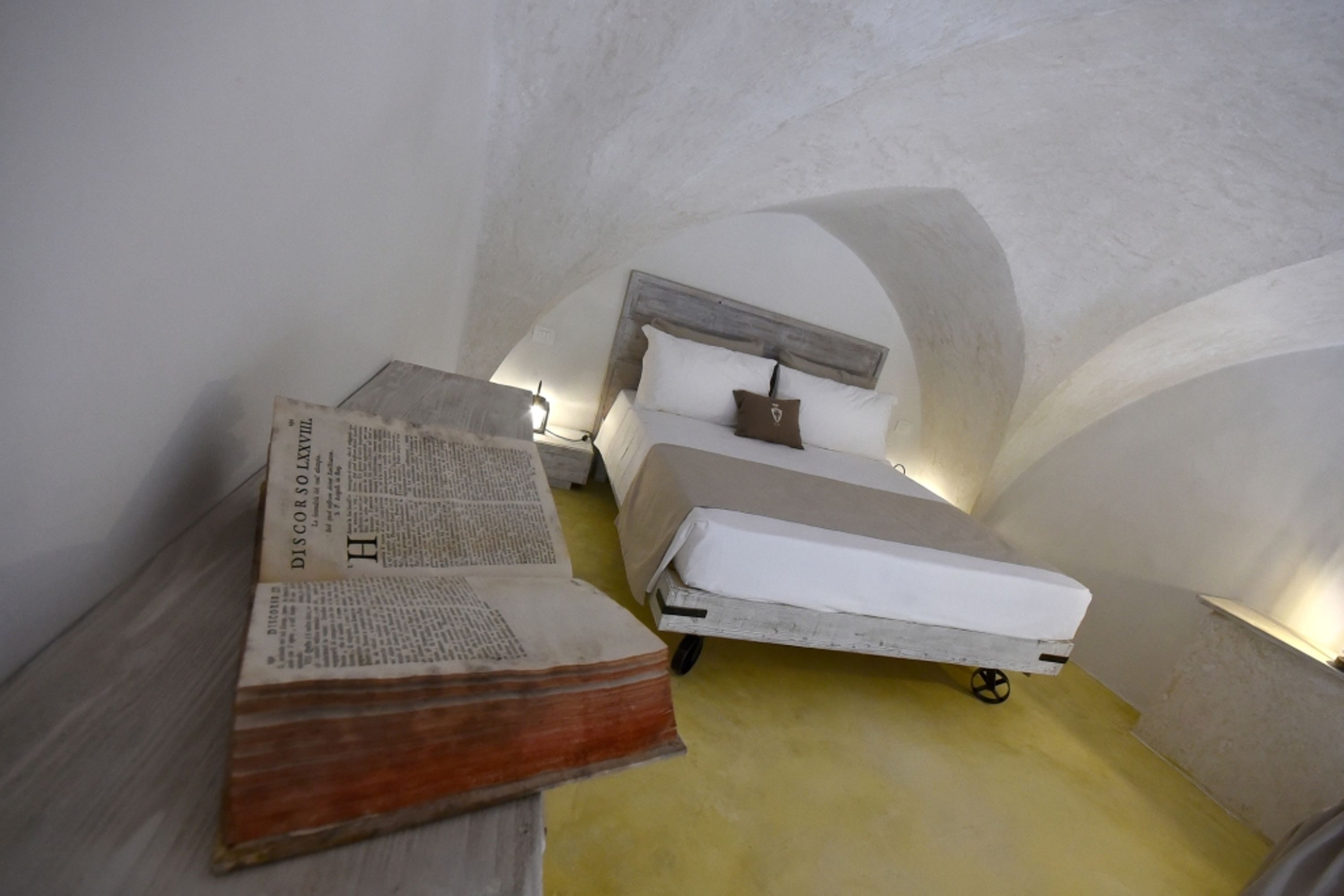 Una habitación pequeña, tenuemente iluminada, con una cama individual y una mesa de madera.