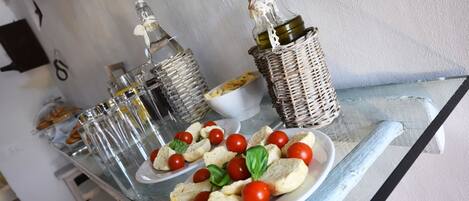 A glass table with plates of bruschetta and cherry tomatoes, surrounded by wicker baskets with glass bottles.