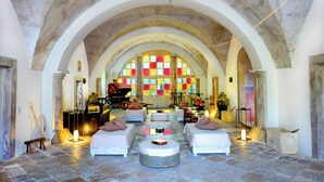 A spacious room with a high arched ceiling, stone flooring, and a central seating area with round tables. - Palazzo Castriota (Alezio)