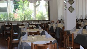 A restaurant with multiple tables set for dining, each with a tablecloth and a folded napkin. - Hotel Corallo (San Mauro Pascoli)