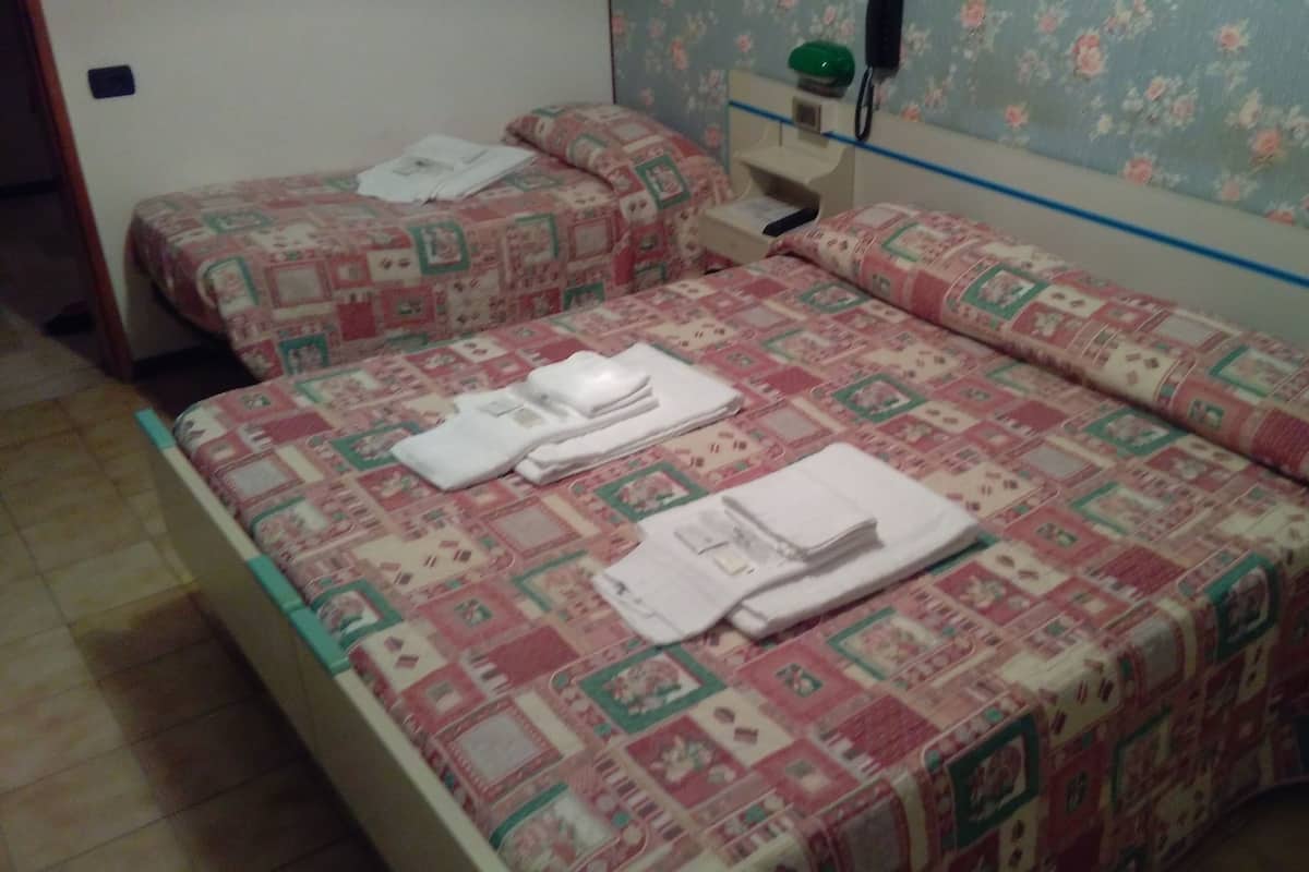 Quarto com duas camas, cada uma com colcha e almofadas estampadas. Pequena mesa de cabeceira com abajur e telefone na parede.