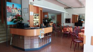A reception area with a counter, chairs, and a dining area with tables and chairs. - Hotel Corallo (San Mauro Pascoli)
