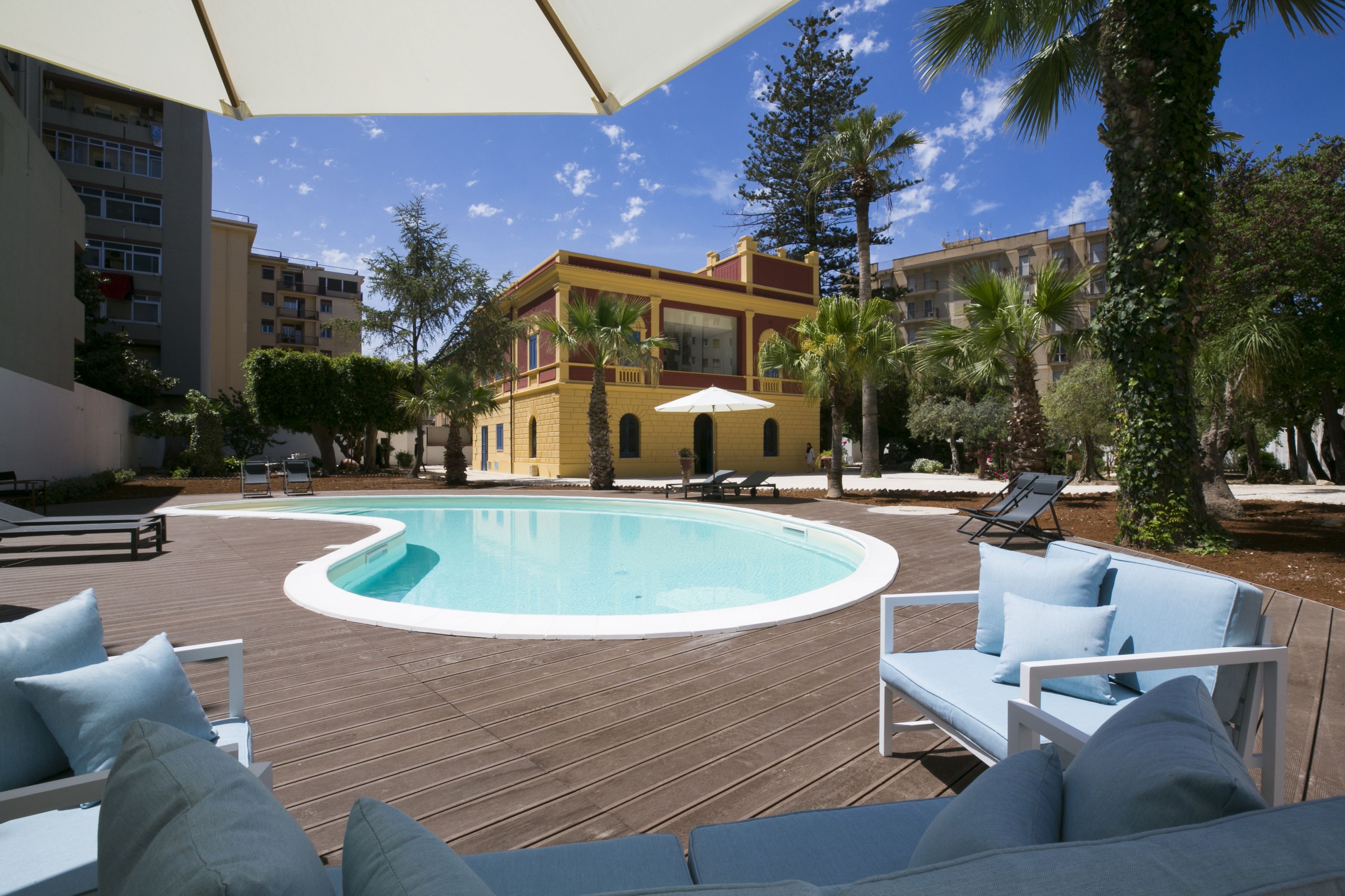A pool area with lounge chairs and umbrellas, surrounded by buildings and palm trees.