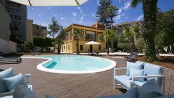 A pool area with lounge chairs and umbrellas, surrounded by buildings and palm trees.