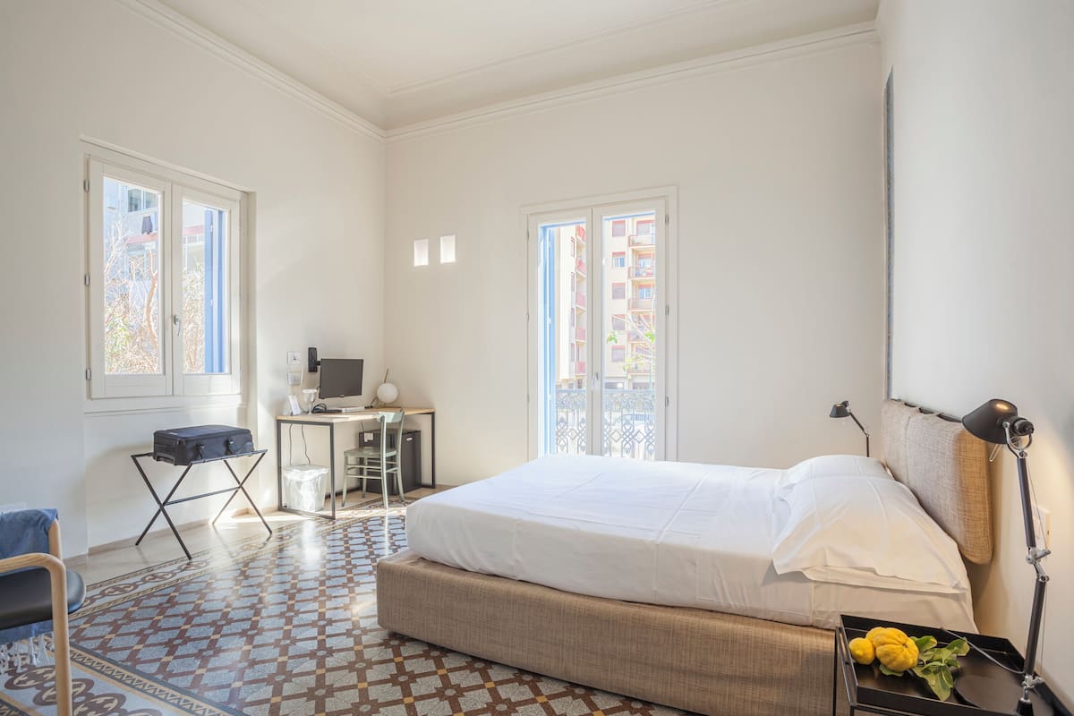 Un dormitorio con cama, escritorio, silla y vistas al exterior por una ventana.