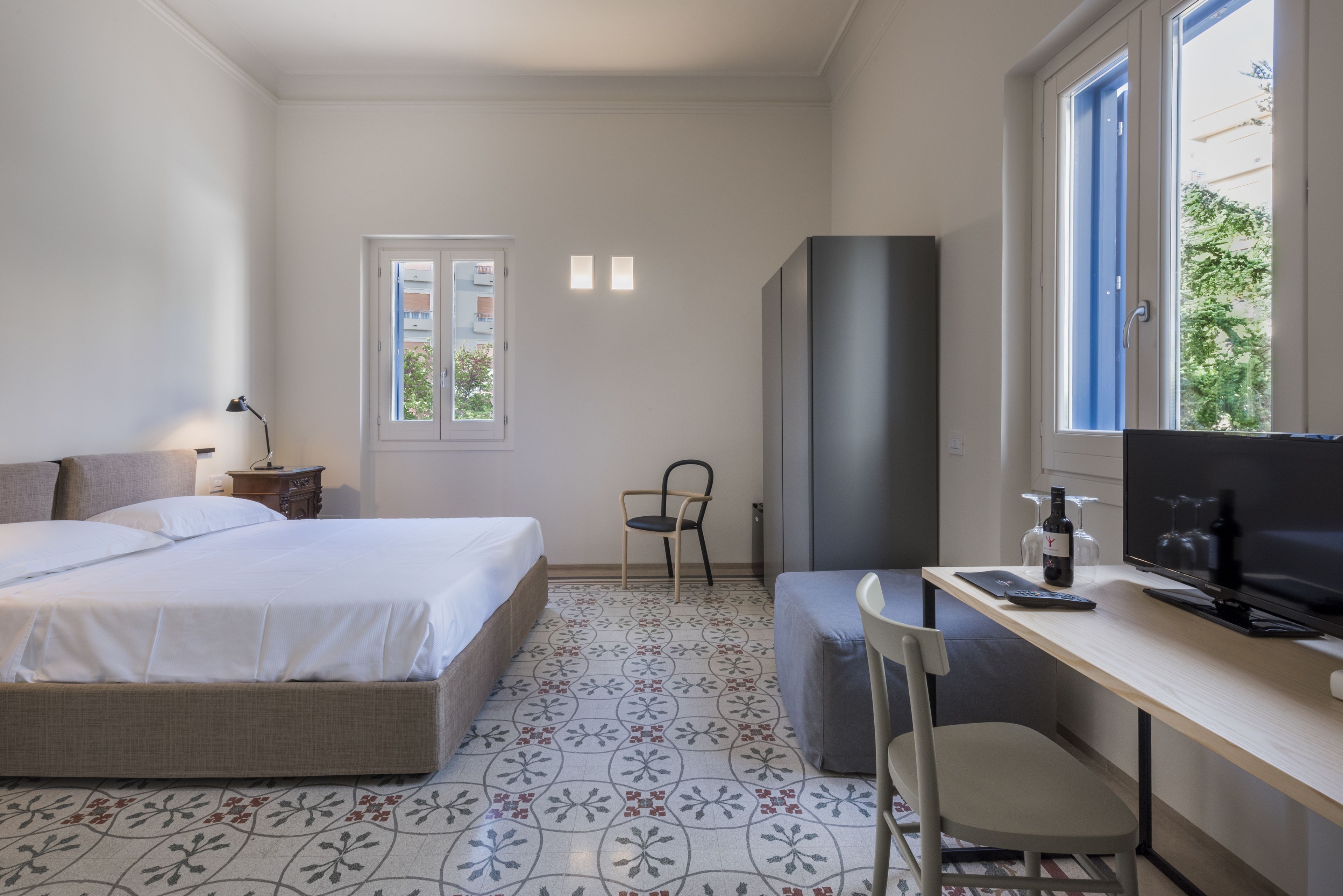 Quarto com cama, escrivaninha com computador, cadeira, televisão e janela.