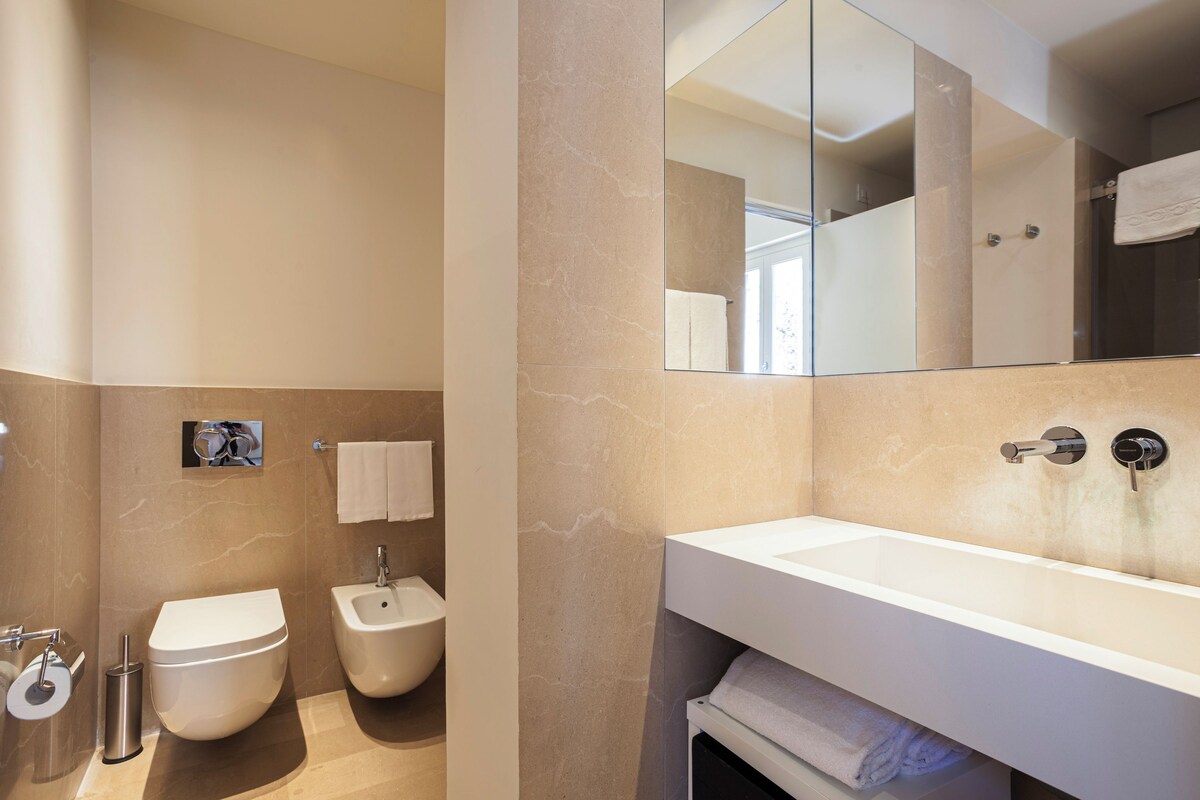 A modern bathroom with a toilet, bidet, and a large mirror above a sink.