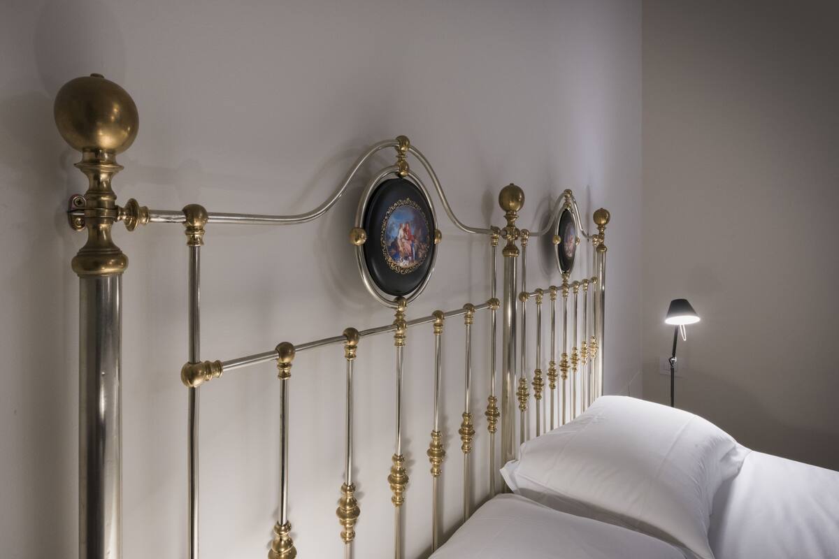 Una cama con cabecera de metal con diseños ornamentales y un cuadro enmarco.
