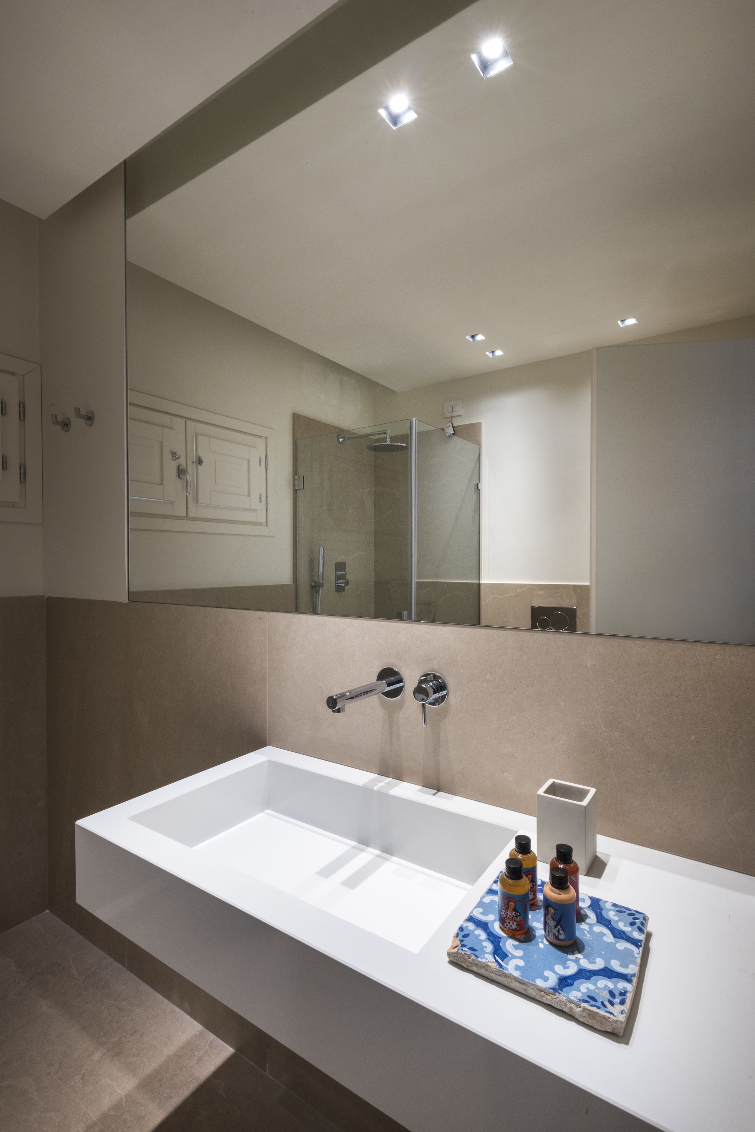 Un bagno moderno con una grande vasca da bagno bianca, uno specchio sopra il lavandino e uno scaffale con articoli da toilette.