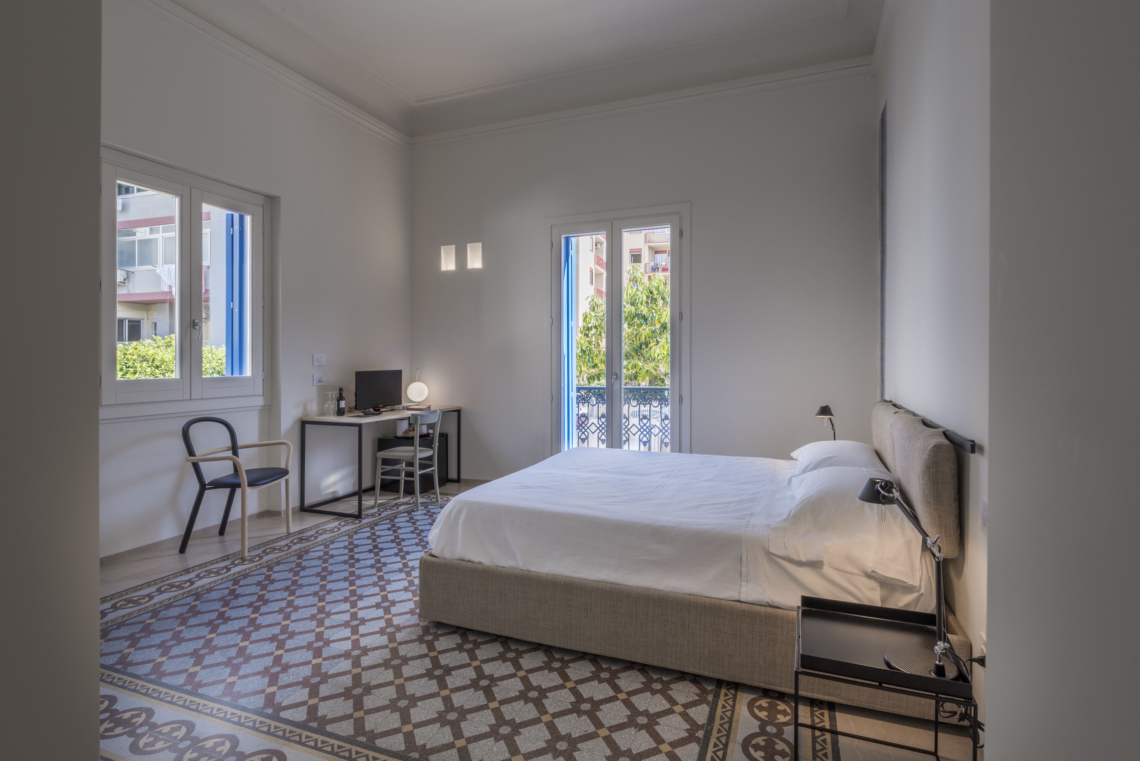 A bedroom with a bed, desk, chair, and a view of the outside through a window.