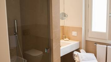 Un baño con ducha de mampara de vidrio, inodoro, lavamanos y carrito con toallas.