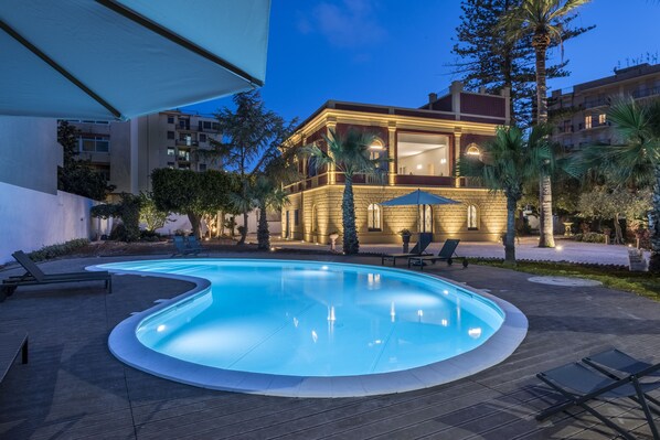 Una piscina al aire libre, sombrillas, sillones reclinables de piscina