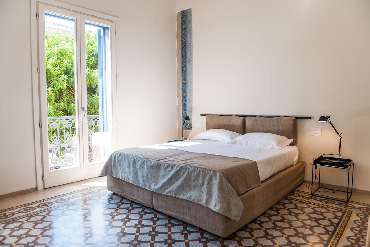 Un dormitorio con una cama, una mesita de noche, una lámpara, un suelo con estampado y una puerta que da a un balcón.