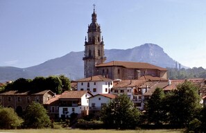 A historic building with a prominent tower, surrounded by residential buildings and a mountainous backdrop. - Casa Rural Kerizara (Otxandio)