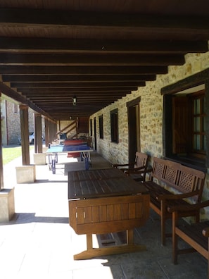 A covered outdoor area with a long table and benches, stone walls, and wooden beams. - Casa Rural Kerizara (Otxandio)