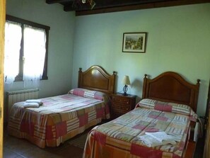 A room with two beds, a window with curtains, a radiator, and a framed picture on the wall. - Casa Rural Kerizara (Otxandio)