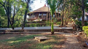 A thatched-roof building surrounded by lush greenery and stone pathways. - Ghion Hotel (Addis Ababa)