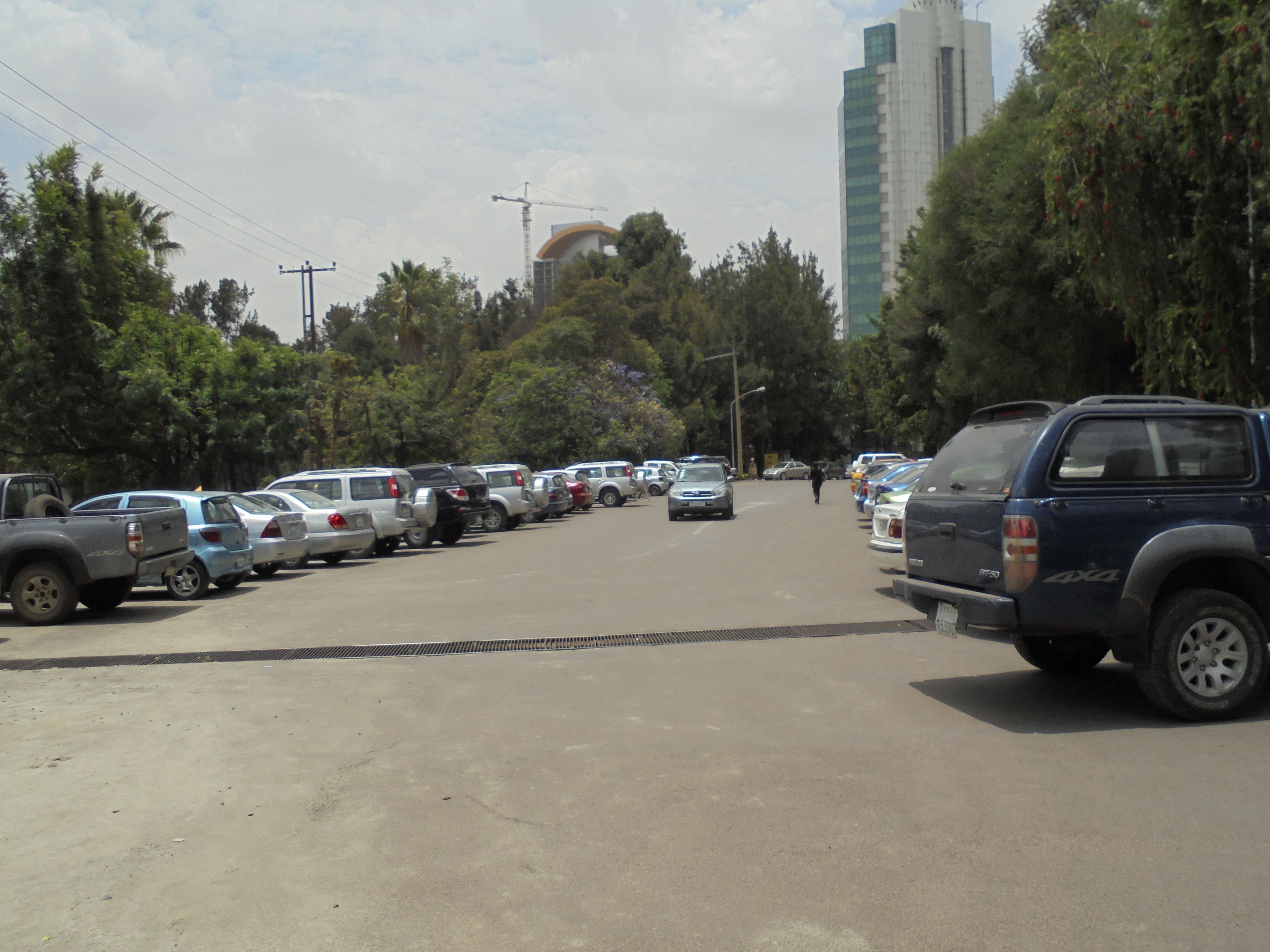 A parking lot with multiple cars and a few people walking.