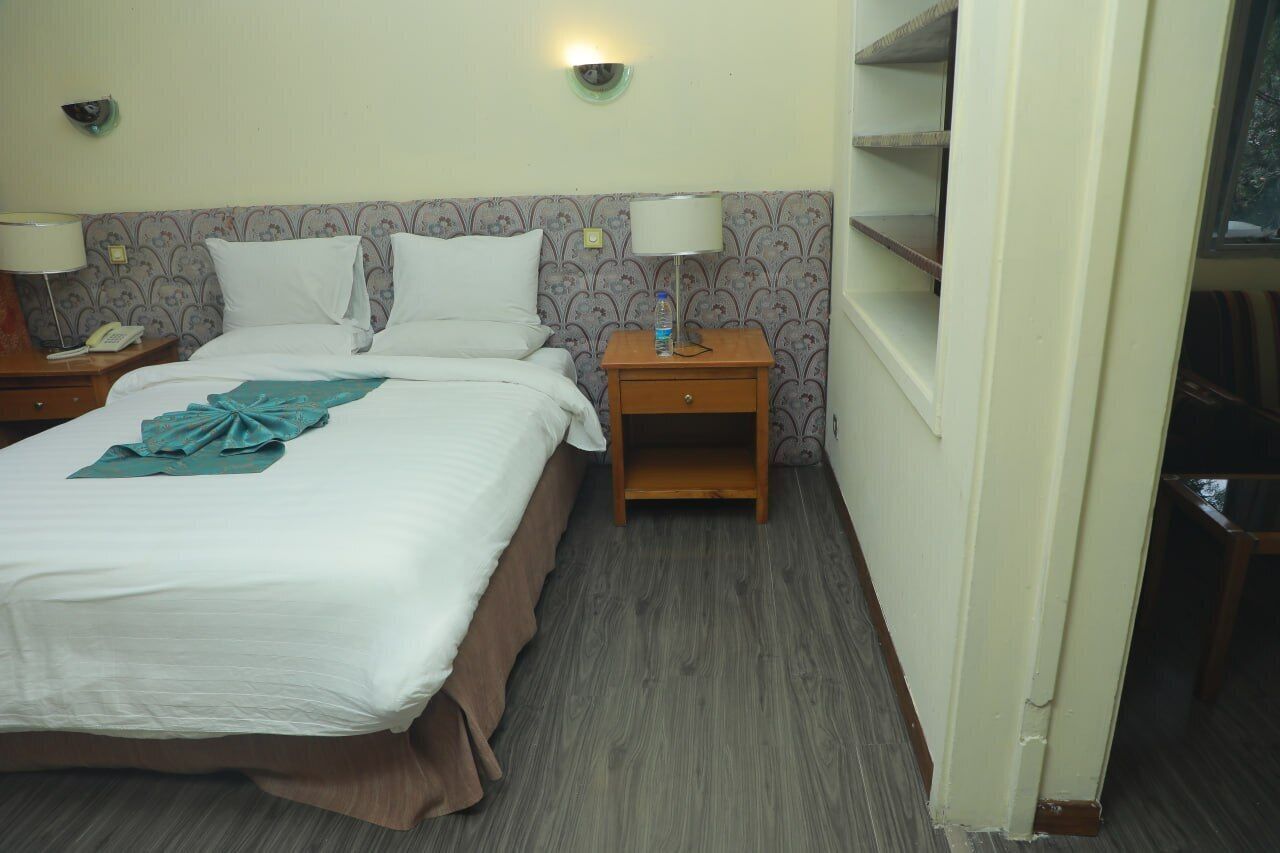 Una habitación de hotel con una cama, dos mesitas de noche, una lámpara y una botella de agua.