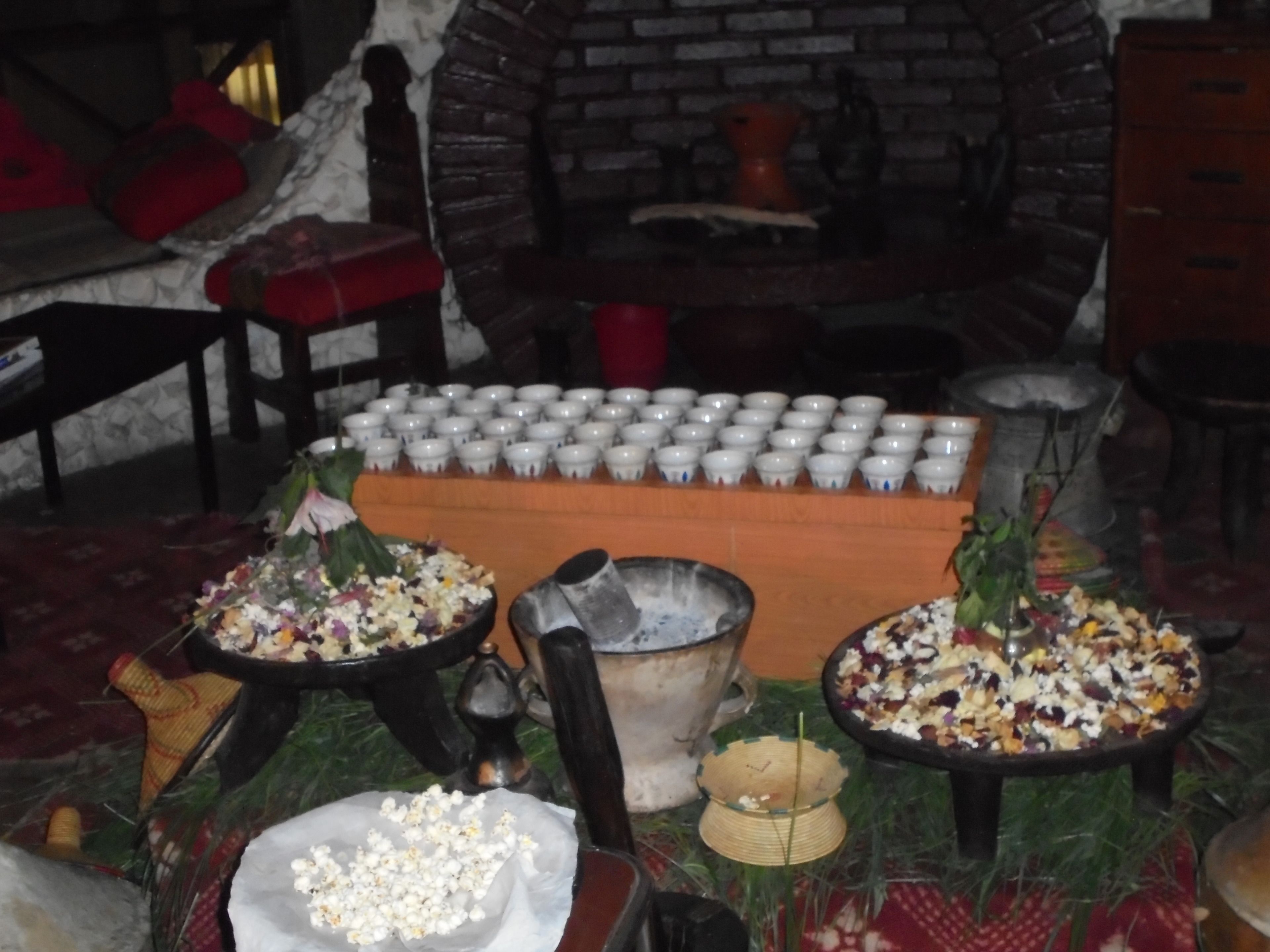Une cuisine traditionnelle avec un four en briques, divers ustensiles de cuisine et une collection de tasses blanches exposées.