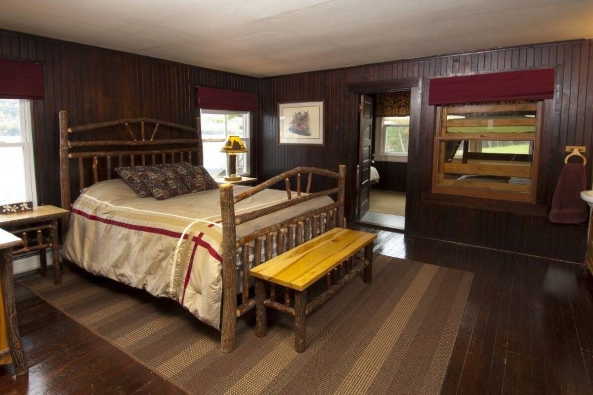 A rustic wooden bed with a bench, a small table, and a window with a view.