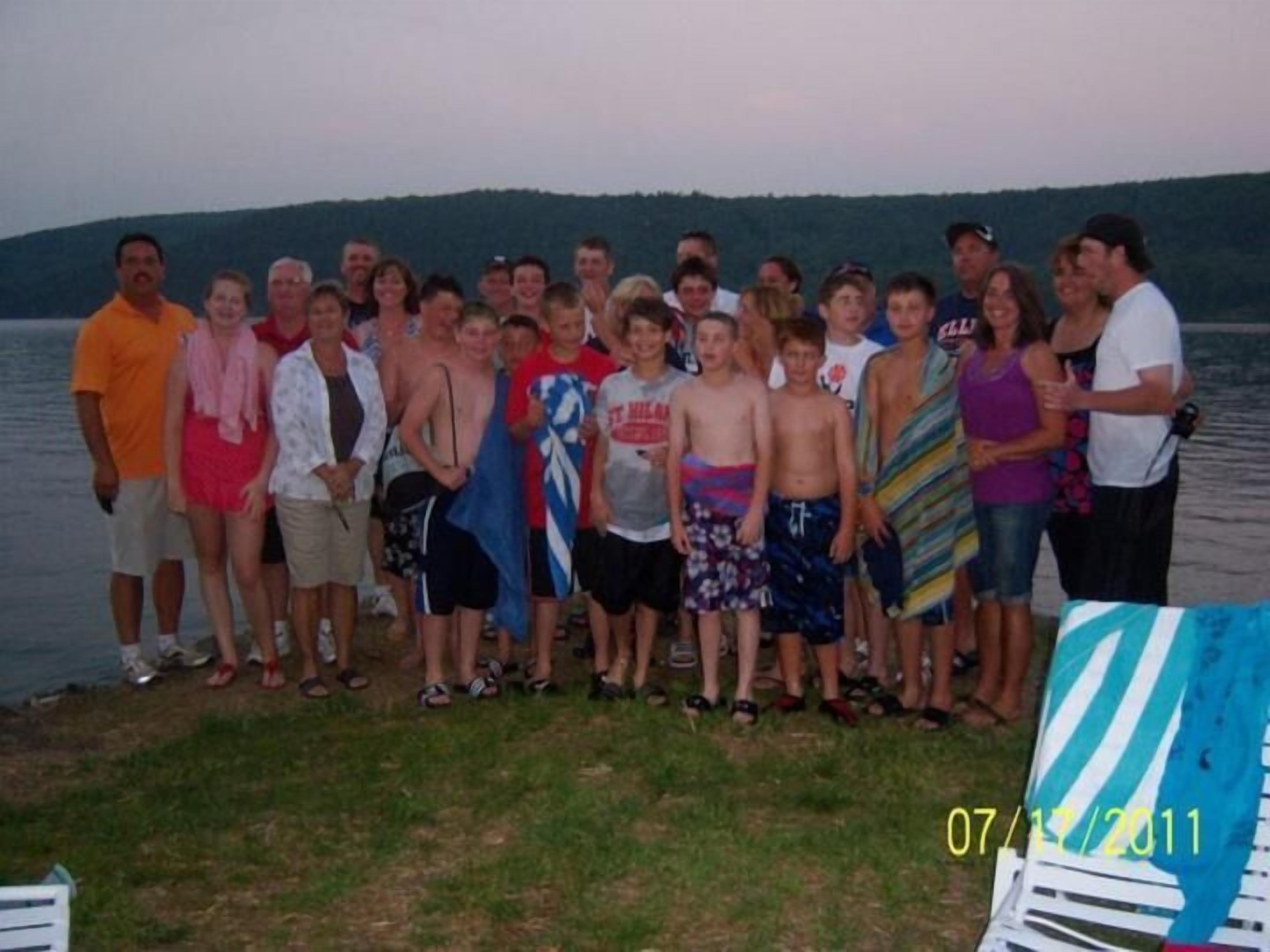 A group of people standing by a lake with a grassy area in the foreground.