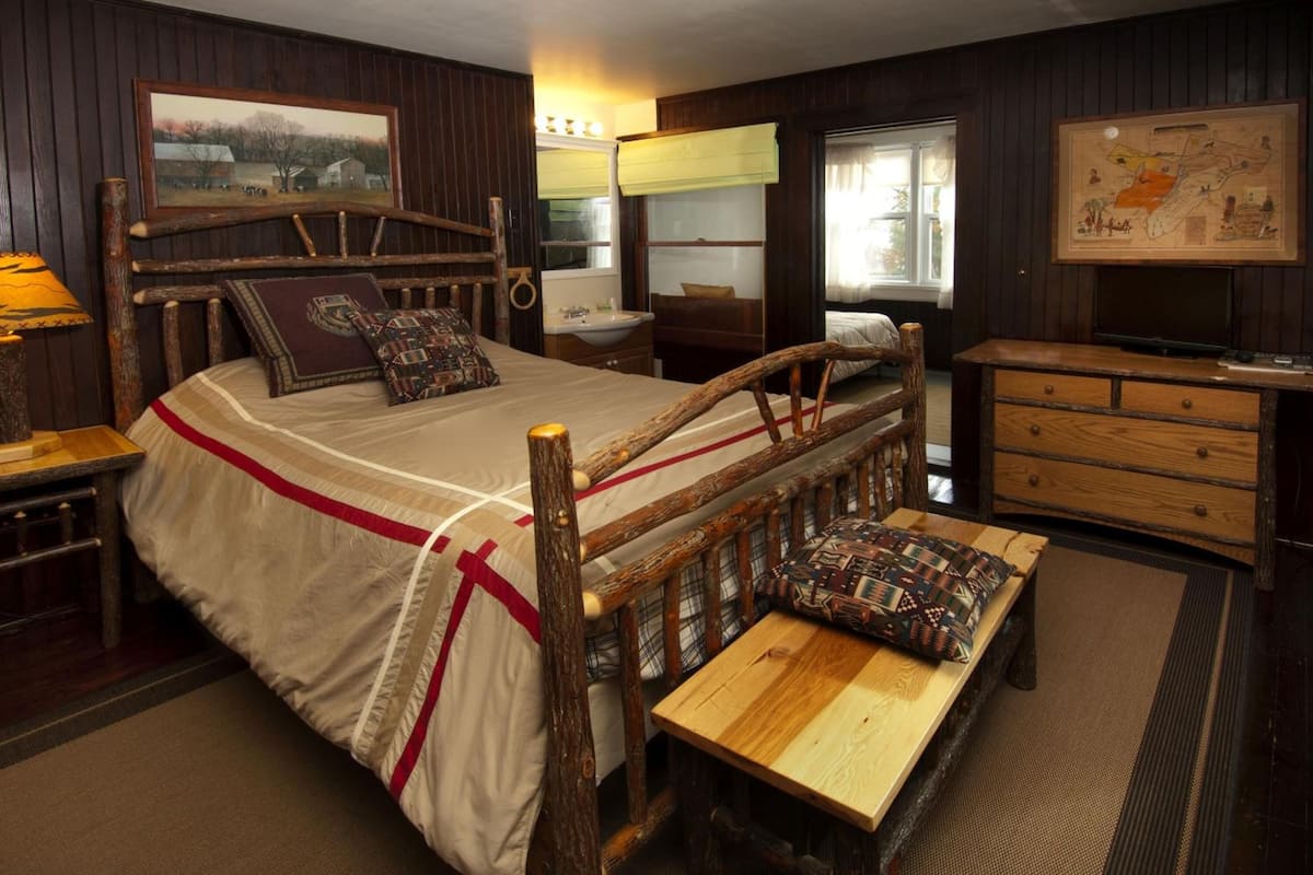 A rustic room with a wooden bed, a wooden bench, a dresser, a mirror, and a map on the wall.