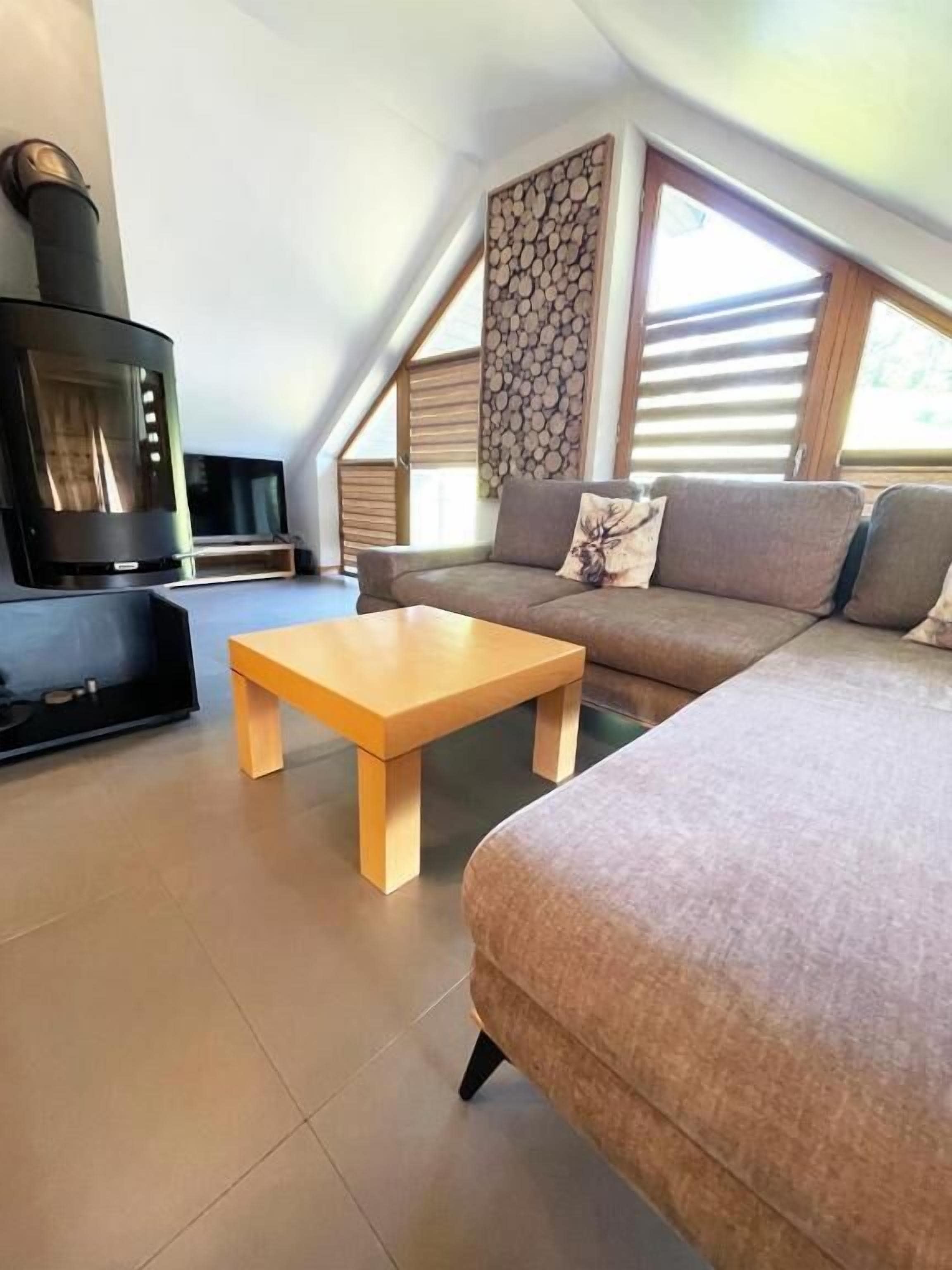 Un salon moderne de style industriel, avec un canapé d’angle, une table basse en bois, un téléviseur à écran plat et un mur en pierre servant d’élément décoratif.