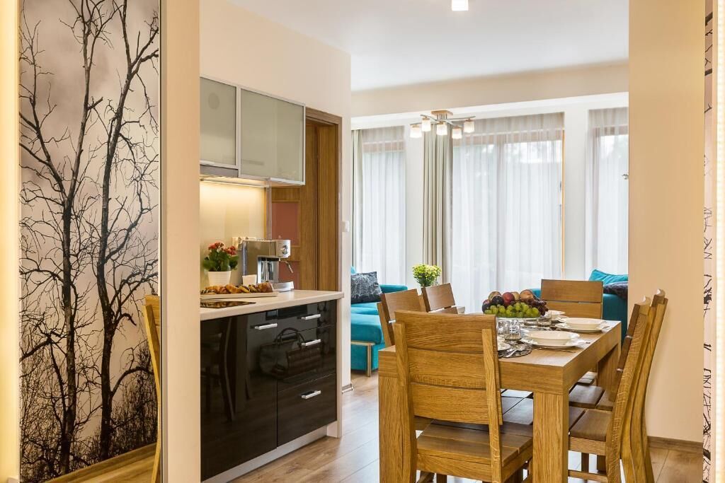 A dining area with a wooden table and chairs, a kitchen with a stove and cabinets, and a living area with a sofa and curtains.