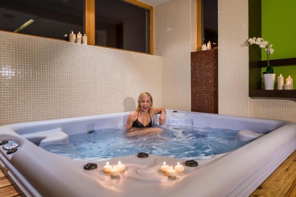 A spa room with a hot tub, candles, and a potted orchid.